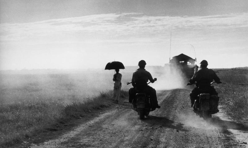 Bassanonet.it - Motorcyclists and woman walking on the road from Nam Dinh to Thai Binh, Vietnam, May 25, 1954  © Robert Capa © International Center of Photography/Magnum Photos